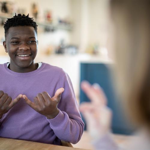 A young boy makes a Sign Language sign that means now, or today. 2 hands palms up, middle three fingers touching palms.