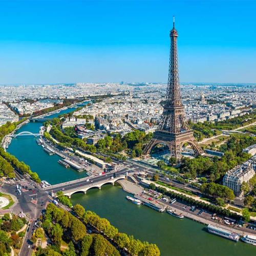 An aerial view of the Eiffel Tower, soaring above tree-lined Parisien streets on the banks of the Seine River.