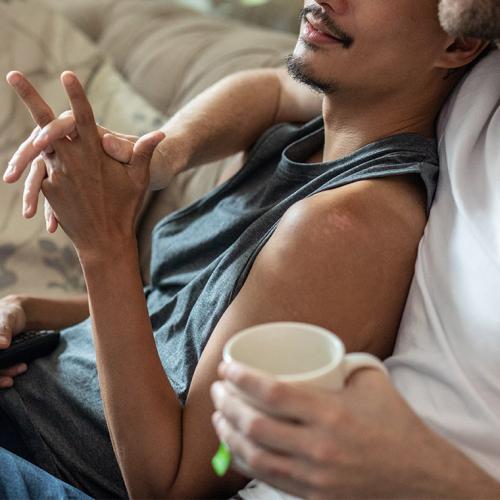 Two men hold hands as one leans comfortably against the other.
