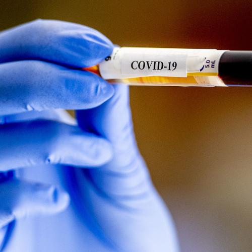 A gloved hand holds a medical vial labelled COVID-19.