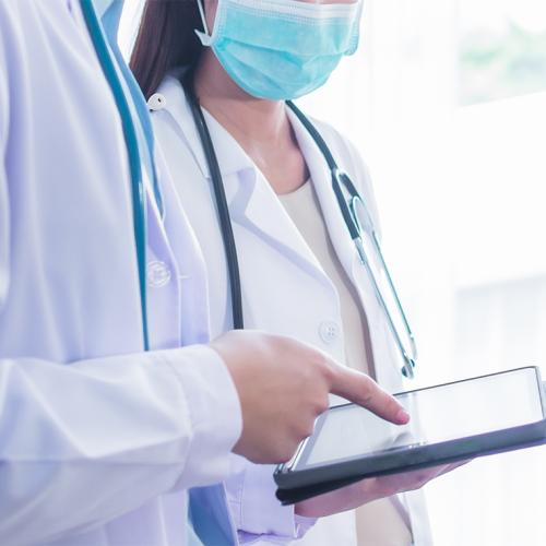 In a stock image, a man and a woman in white doctor's coats look at a tablet together.