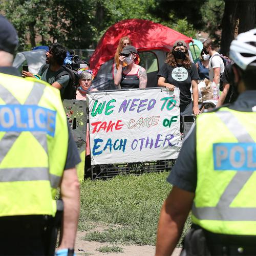 Police face protesters holding a sign that reads: We need to take care of each other.
