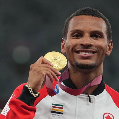 Andre De Grasse smiles as he holds up an Olympic gold medal.