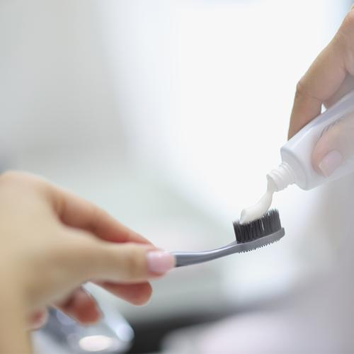 A close-up of a person's hands as they squeeze toothpaste onto a toothbrush.
