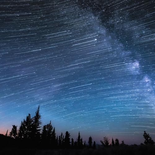 In a time-lapse image, thousands of stars appear as streaks of light across a dark sky and the cloudy line of the Milky Way.