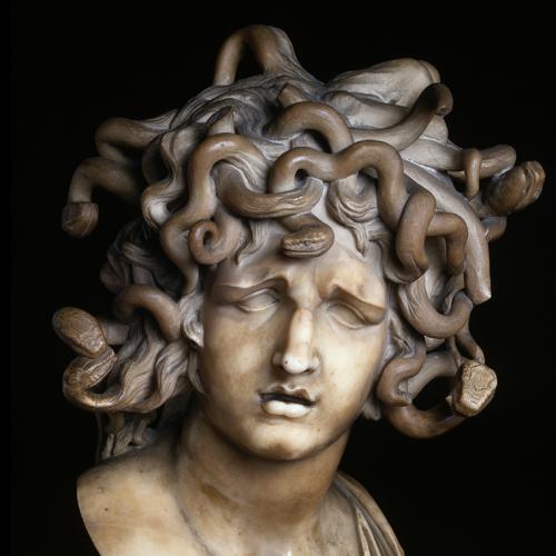 An ancient stone statue of Medusa shows a woman with no eyes and hair made of writhing snakes.