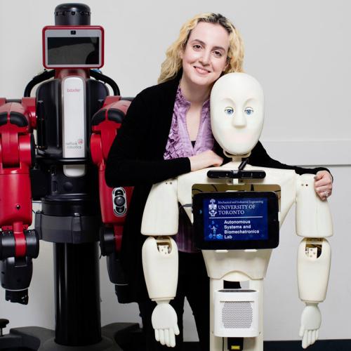 Goldie Nejat stands with a human-shaped robot. Text on the robot’s chest: Autonomous Systems and Biomechatronics Lab.