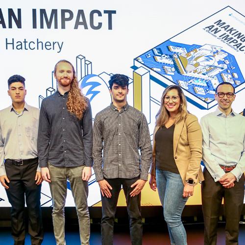 Seven people stand in front of a screen at Hatchery Demo Day. Text reads: making an impact.