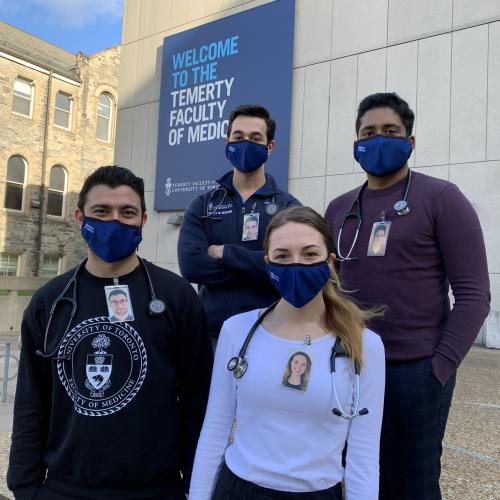 Damoon Ghahari, James Sanayei, Caroline Gregory and Rayoun Ramendra wear masks and laminated photos of themselves smiling.