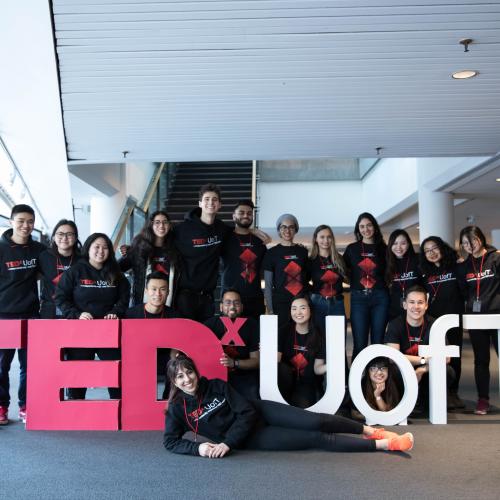 A large group of happy students in matching t-shirts pose with a big sign: TEDx U of T.