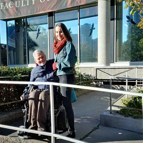Ian Parker smiles as he poses in his wheelchair on a ramp, with his arm around his daughter Emily Parker (who is standing).
