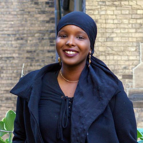 Ikran Jama smiles while standing in a garden outside a stone building.