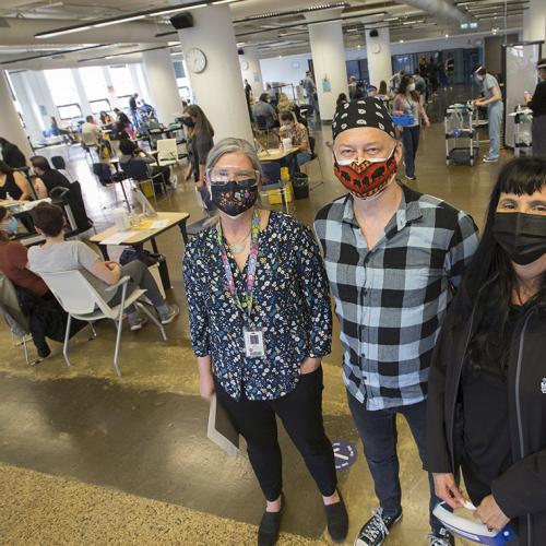Janet Smylie, Michael Anderson and Suzanne Stewart, wearing masks, stand in an atrium dotted with vaccination stations.
