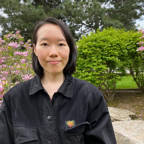 Irene Fang stands outside with trees and flowers around her