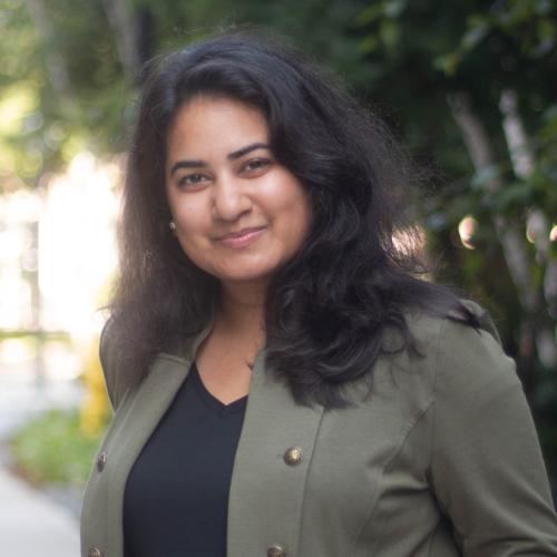 Ishita Aggarwal smiles, standing on a sunny sidewalk outdoors.