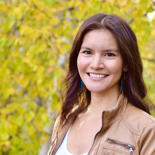 Itoah Scott-Enns smiles, standing outdoors by birch trees.