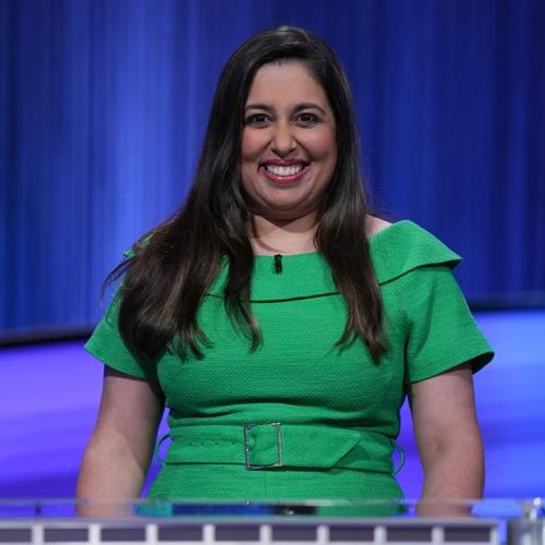 Javeria Zaheer wearing a green dress and smiling on the Jeopardy! set.