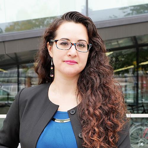 Jennifer Brant looks serious as she stands on a sidewalk in front of a building.