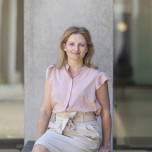 Jennifer Gommerman smiles, sitting in front of a concrete pillar outdoors.
