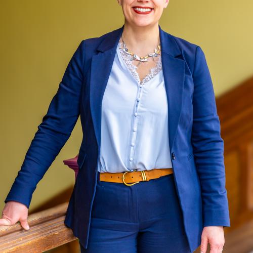 A woman wearing a blue suit standing in front of a bright yellow wall. 