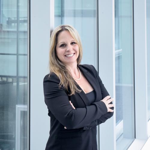 Julie McCarthy smiles, standing in a glass-walled walkway.