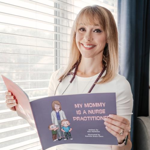 Kim standing by a window holding her book open and smiling