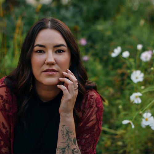 Karen McBride leans forward and looks serious in a meadow with wildflowers.