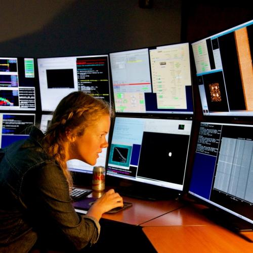 Katie Harris works in front of a bank of eight computer monitors, all displaying different information.