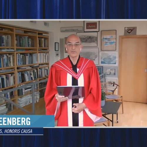Ken Greenberg, wearing academic robes, speaks in a room decorated with bookshelves, paintings, and carved masks.