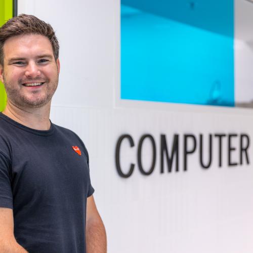 Kent Fenwick smiles for the camera next to a sign that says Computer Science.