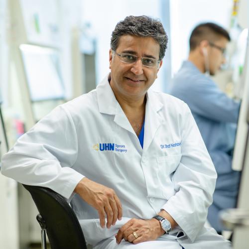 Shaf Keshavjee smiles, wearing a lab coat with the logo: UHN Sprott Surgery