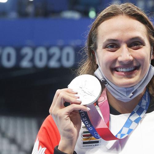 Kylie Masse smiles as she holds up her Olympic silver medal. A banner behind her reads: Tokyo 2020.