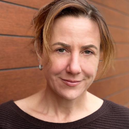 Lisa Hepner smiles, standing by a brick wall.