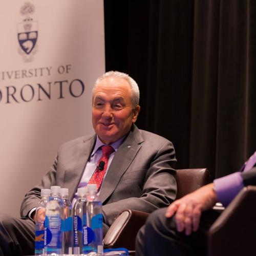 Lorne Michaels smiles and talks, sitting in a chair on a stage. A sign behind him reads, University of Toronto.