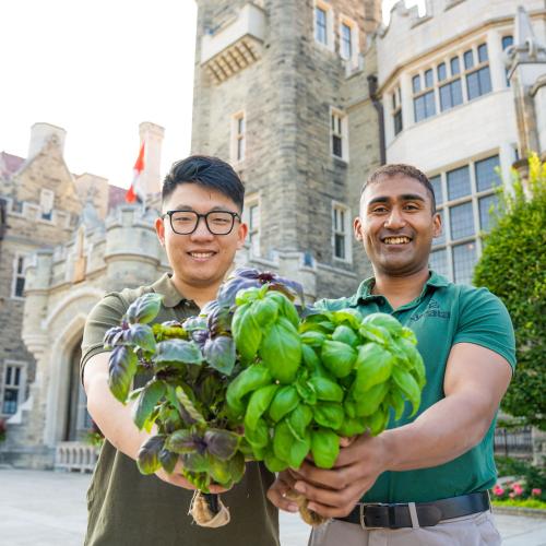 Leo and Adnan holding basil plants in front of the Casa Loma building