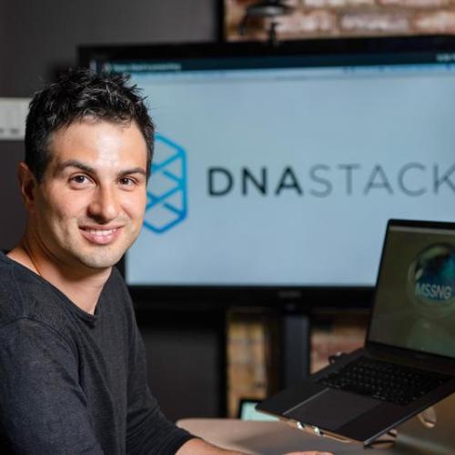 Marc Fiume smiles as he looks away from an array of computer monitors displaying the logo of his company DNAstack.