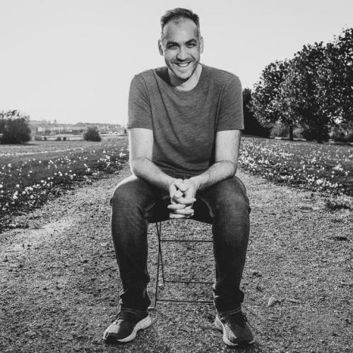 Mark Crawford sitting on a stool in the middle of a field, laughing.