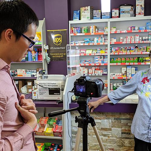 Michael Do sets up a camera to film a pharmacist, who stands in front of her counter in a drug store.