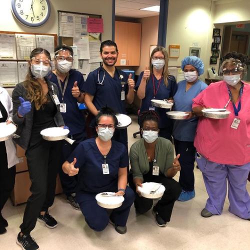 A group of hospital workers in masks, gloves and scrubs hold out trays of delivered meals.