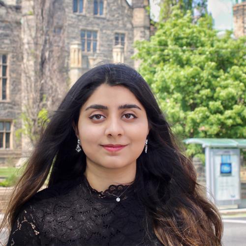 Sara Imran smiles quietly while standing on a sunny street.