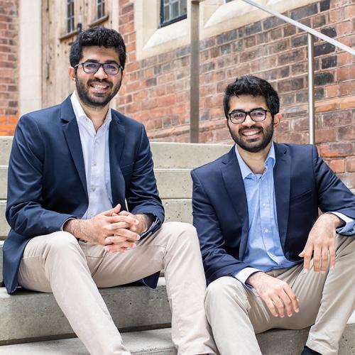 Nishul and Nakul Juneja, dressed identically, laugh as they sit on steps outside a building.
