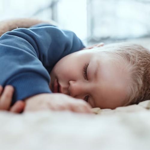 A baby in a blue sweatshirt sleeping on its side