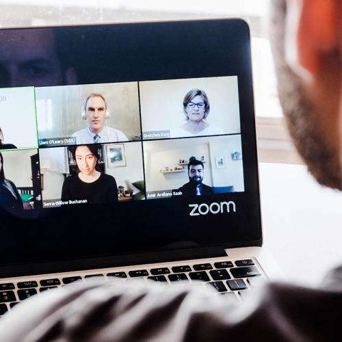 A man looks at a laptop which is running a video chat application with six other users.