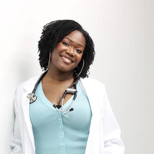 Onye Nnorom leans against a wall, smiling, wearing lab coat and stethoscope.