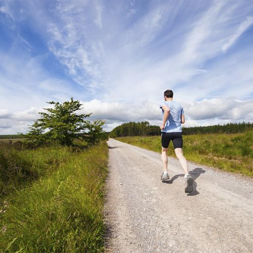 A man jogs along an empty country road under a wide sunny sky.
