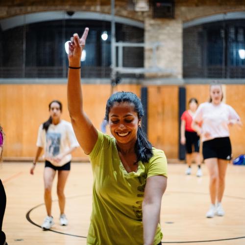 Sandani Hapuhennedige smiling in a gymnasium as she teaches a fitness class to others.