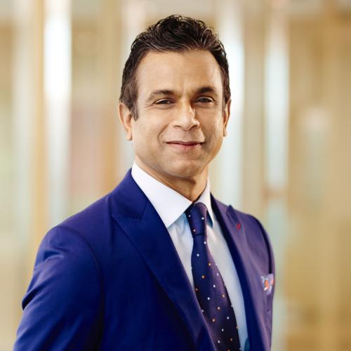 A portrait of Ramesh wearing a blue suit and tie