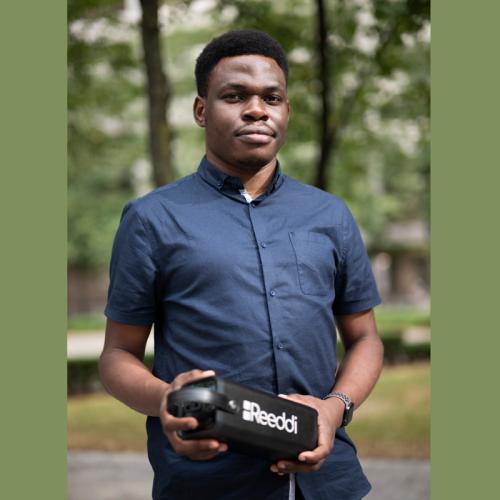 Olugbenga Olubanjo stands outside by trees, holding a loaf-sized, rectangular box with the word Reeddi on the side.