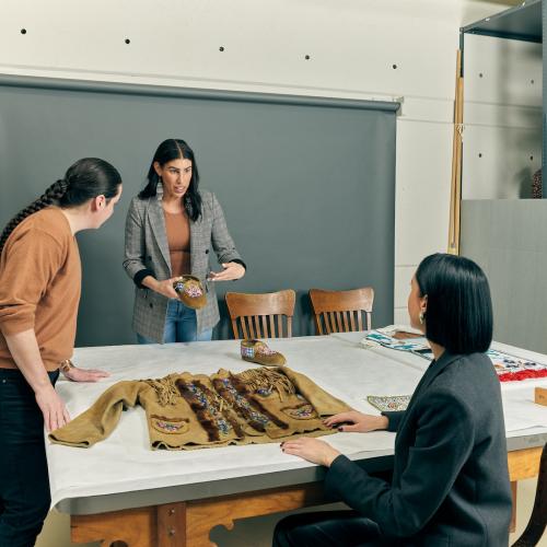Three people at a large table with traditional Indigenous garments on it 