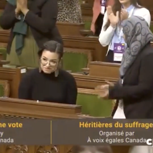 In Ottawa's House of Commons, women stand and applaud Riley Yesno. Caption reads: Daughters of the vote, Equal Voice Canada.
